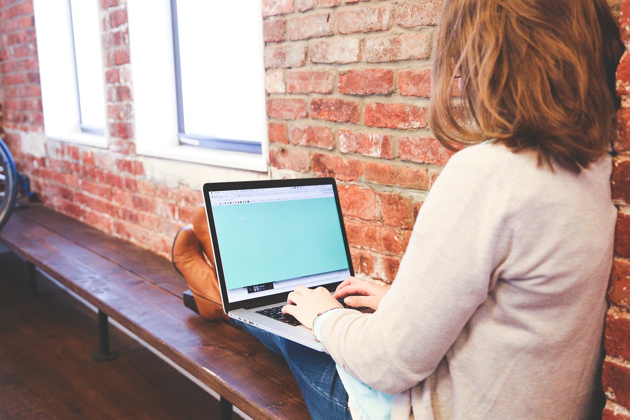 A student is sitting on a bench typing on a laptop. 